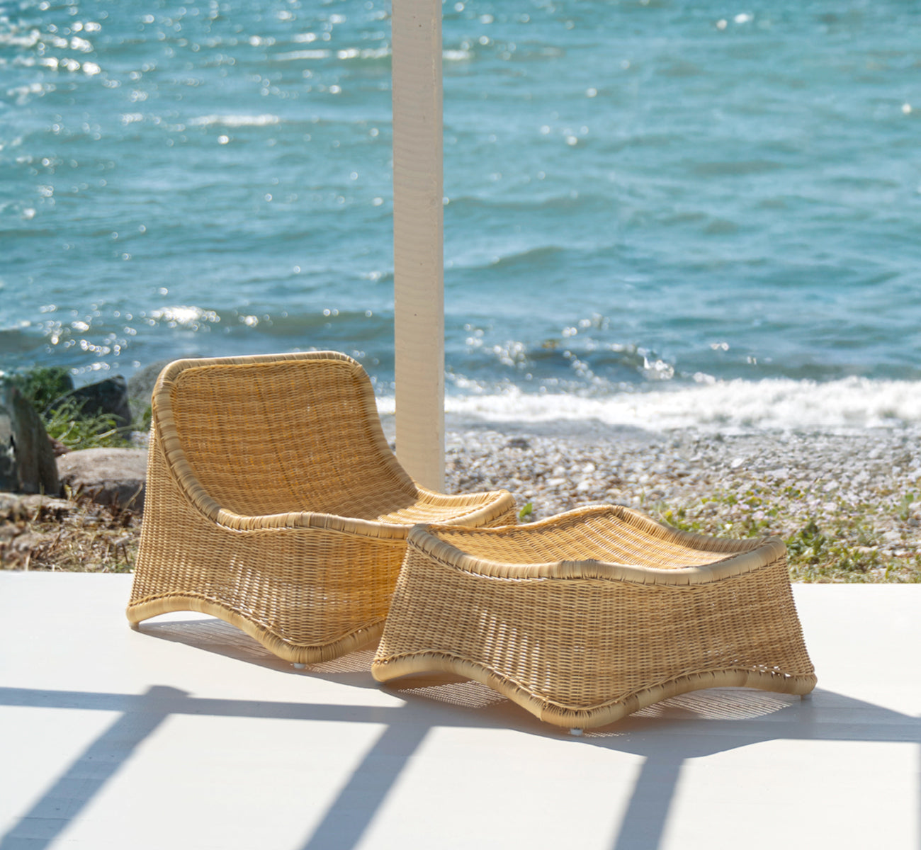 Esta es una imagen de estilo de vida de Chill sillón lounge en natural core weave ArtFibre Aluminium, en una terraza de madera junto al agua con.