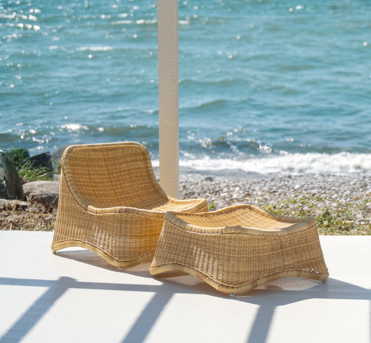 Esta es una imagen de estilo de vida de Chill sillón lounge en natural core weave ArtFibre Aluminium, en una terraza de madera junto al agua con.