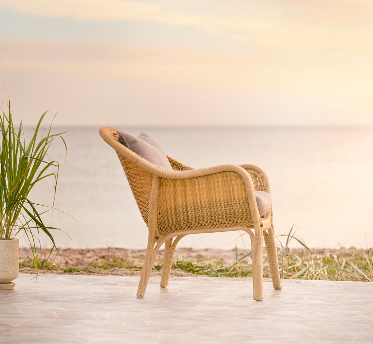 Esta es una imagen de estilo de vida de Madame sillón lounge en natural core weave ArtFibre Aluminium, en una terraza costera abierta al atardecer.