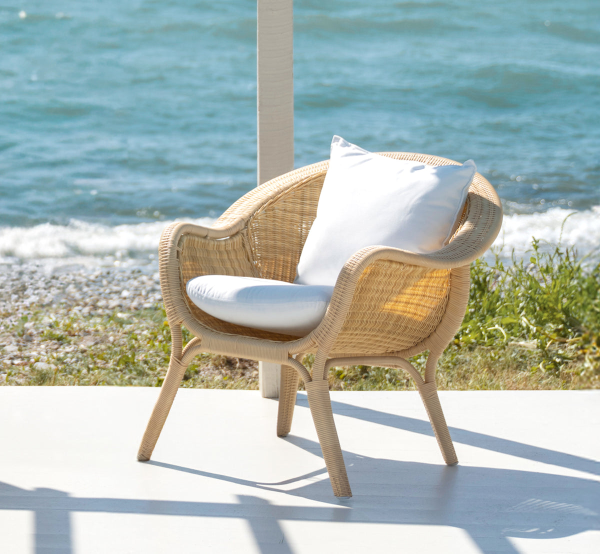 Esta es una imagen de estilo de vida de Madame sillón lounge en natural core weave ArtFibre Aluminium, en una terraza costera abierta al atardecer.