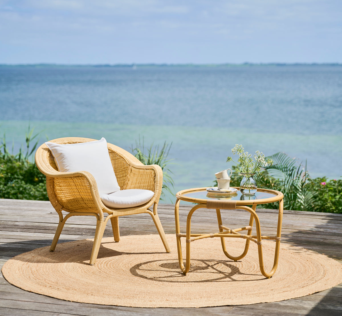 Esta es una imagen de estilo de vida de Madame sillón lounge en natural core weave ArtFibre Aluminium, en una terraza costera abierta al atardecer.