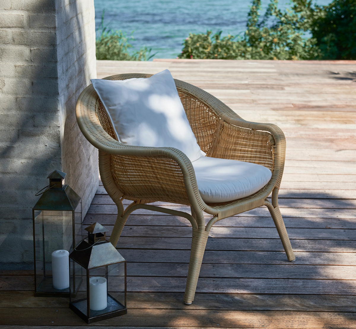 Esta es una imagen de estilo de vida de Madame sillón lounge en natural core weave ArtFibre Aluminium, en una terraza costera abierta al atardecer.