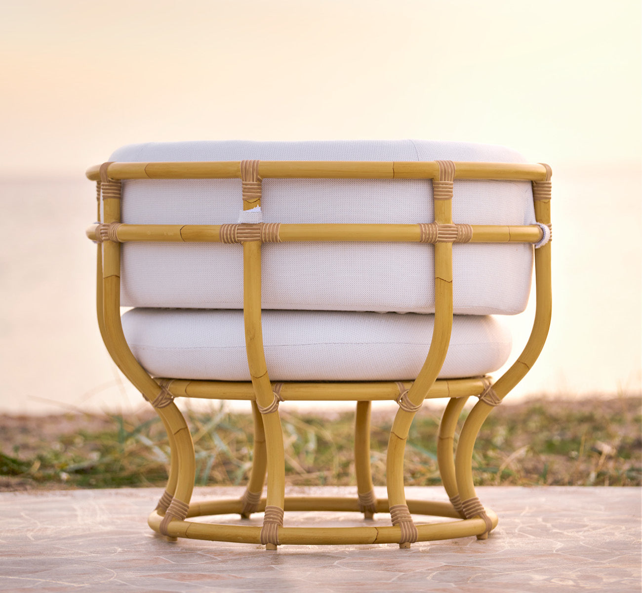 Esta es una imagen de estilo de vida de Coco sillón lounge exterior en natural Aluminium ArtFibre, en una terraza costera abierta al atardecer con.