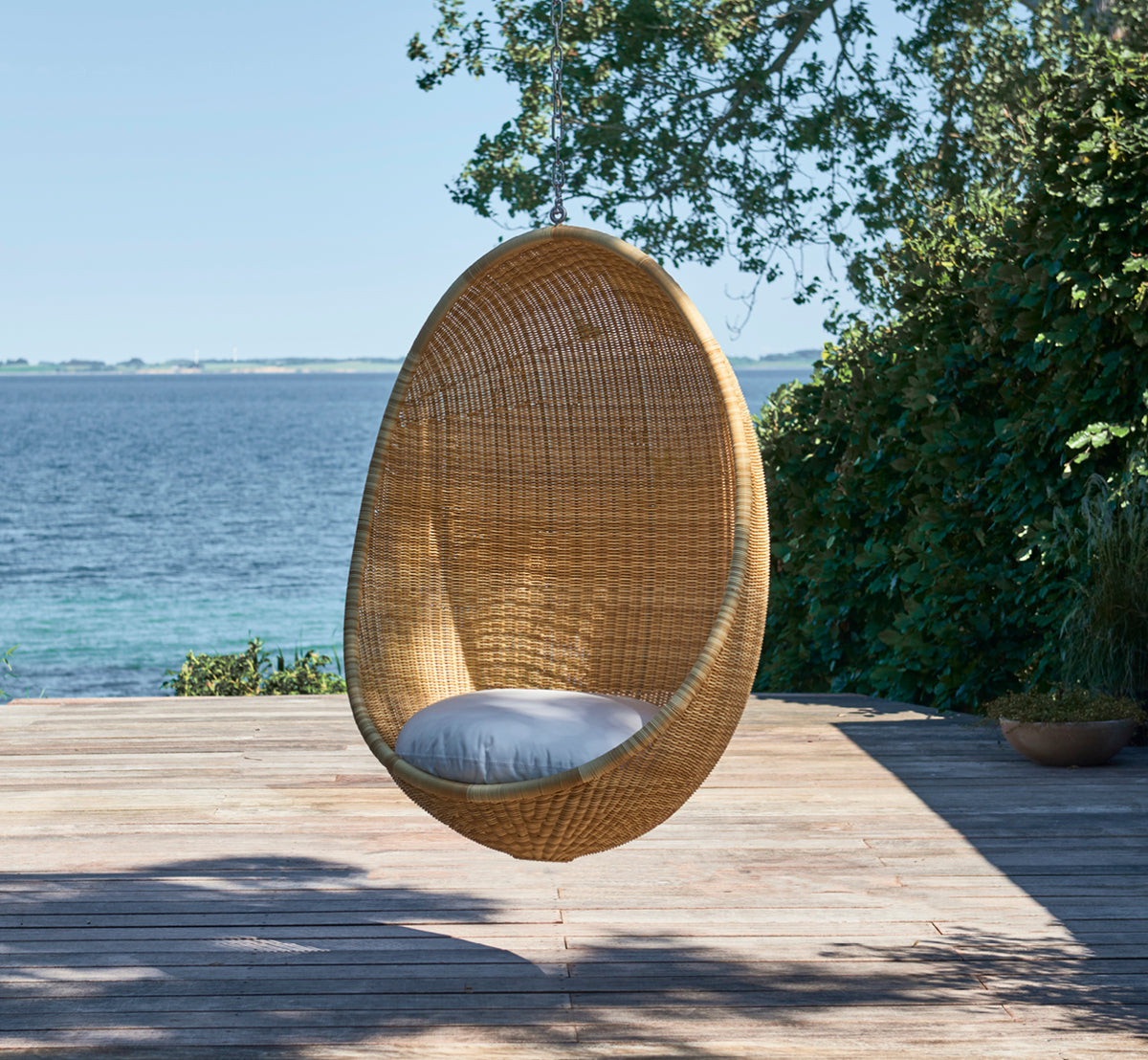 Esta es una imagen de estilo de vida de Hanging silla colgante exterior en natural core weave ArtFibre Aluminium, colgado de una pérgola blanca con.