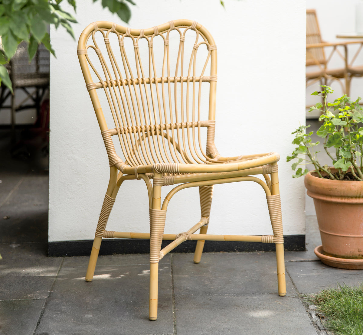 Esta es una imagen de estilo de vida de Margret silla de comedor exterior en natural aluminium artfibre. Patio blanco con macetas de terracota y plantas.