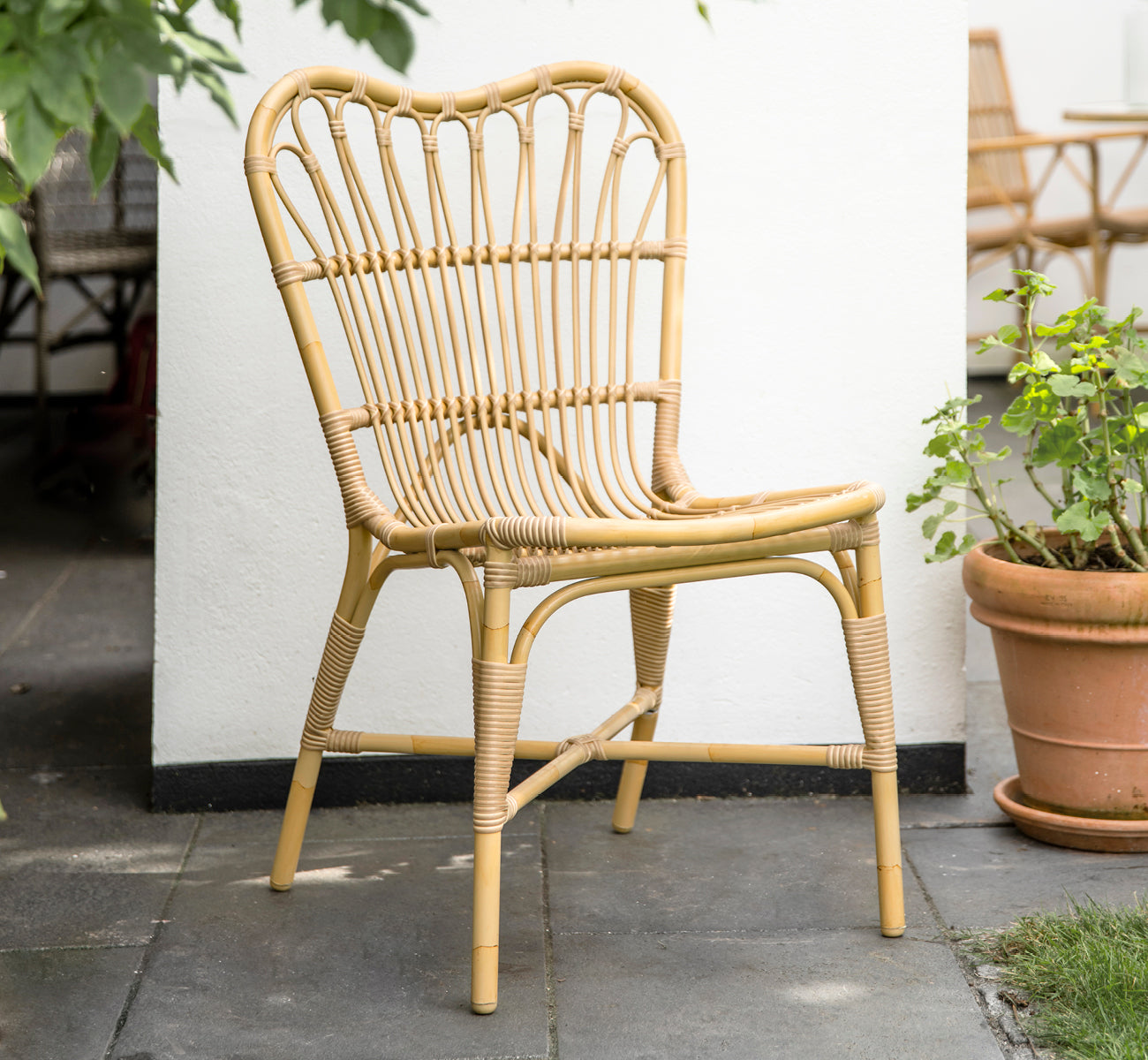 Esta es una imagen de estilo de vida de Margret silla de comedor exterior en natural aluminium artfibre. Patio blanco con macetas de terracota y plantas.