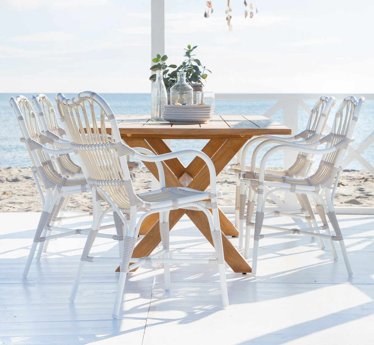 Esta es una imagen de estilo de vida de Margret sillón de comedor exterior en dove white aluminium artfibre. Terraza de playa con mesa de teca y decoraciones.