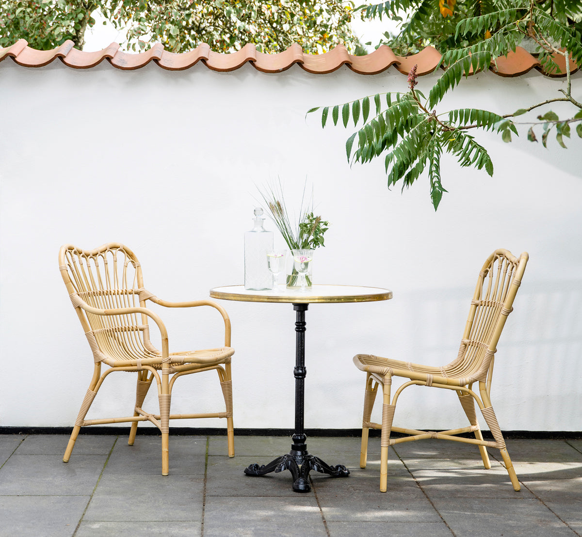Esta es una imagen de estilo de vida de Margret sillón de comedor exterior en natural aluminium artfibre. Patio con mesa de café bajo alero de techo de tejas.