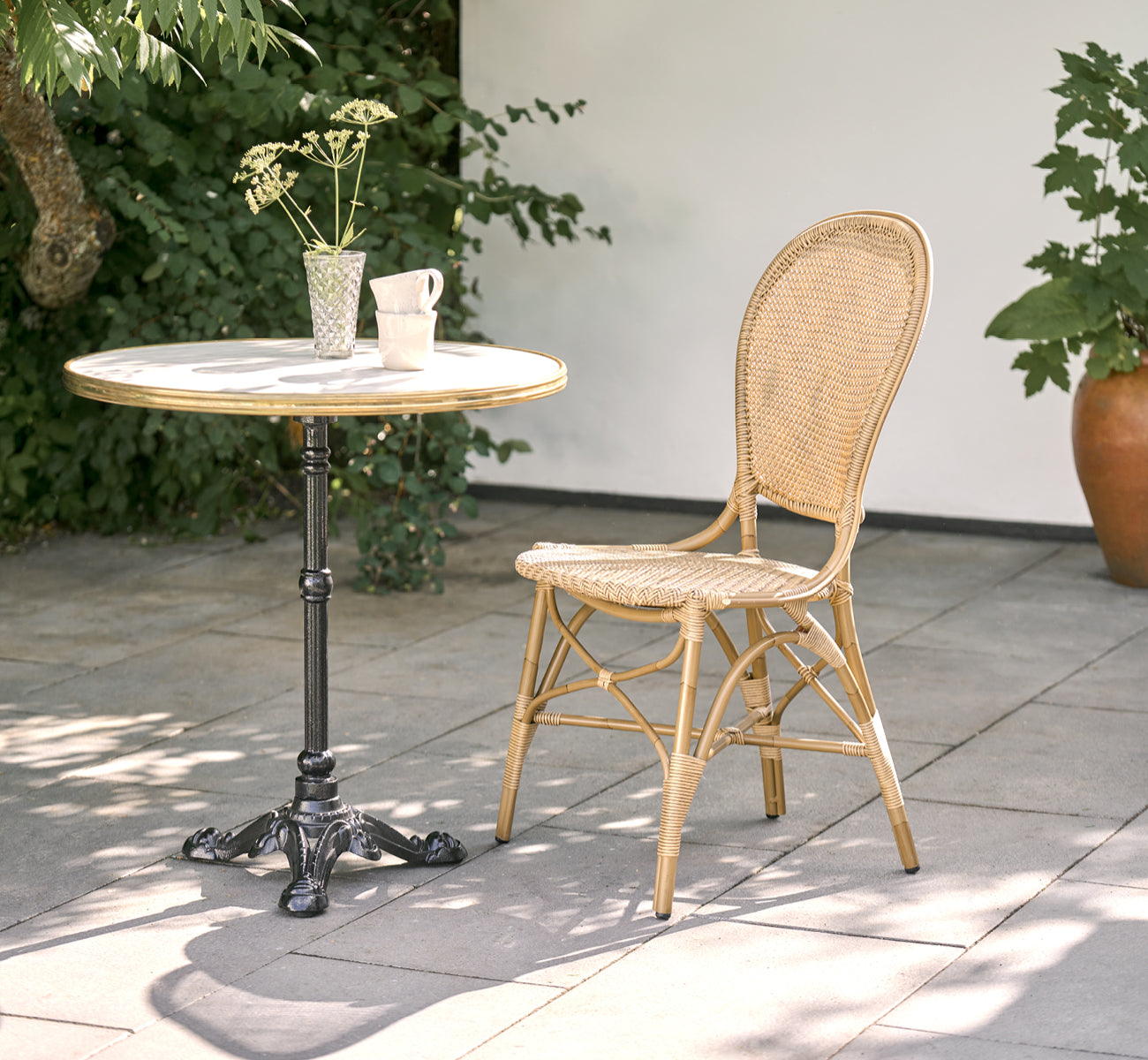 Esta es una imagen de estilo de vida de Rossini silla de comedor exterior en antique aluminium artfibre. Estilizado en un interior luminoso.