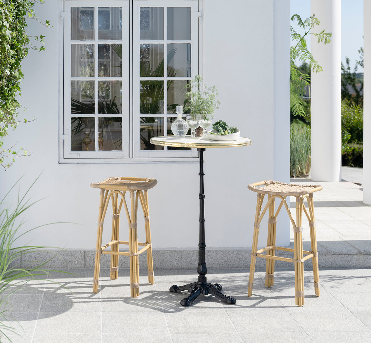 Esta es una imagen de estilo de vida de Salsa taburete alto de bar exterior en natural aluminium artfibre. Elegante patio con mesa de bar y plantas verdes.