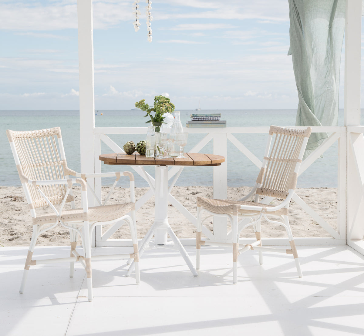 Esta es una imagen de estilo de vida de Piano Exterior Dining Armchair i dove white aluminium artfibre. En una pérgola junto al mar con vista al océano.