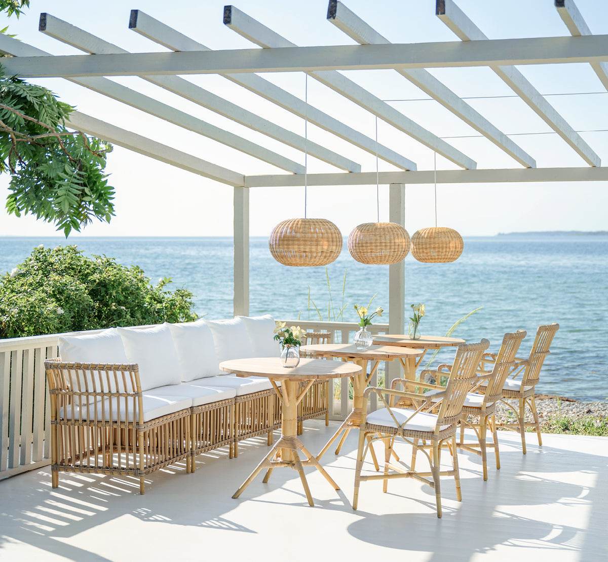 Esta es una imagen de estilo de vida de Piano Exterior Dining Armchair i natural aluminium artfibre. En una pérgola junto al mar con lámparas colgantes de ratán.