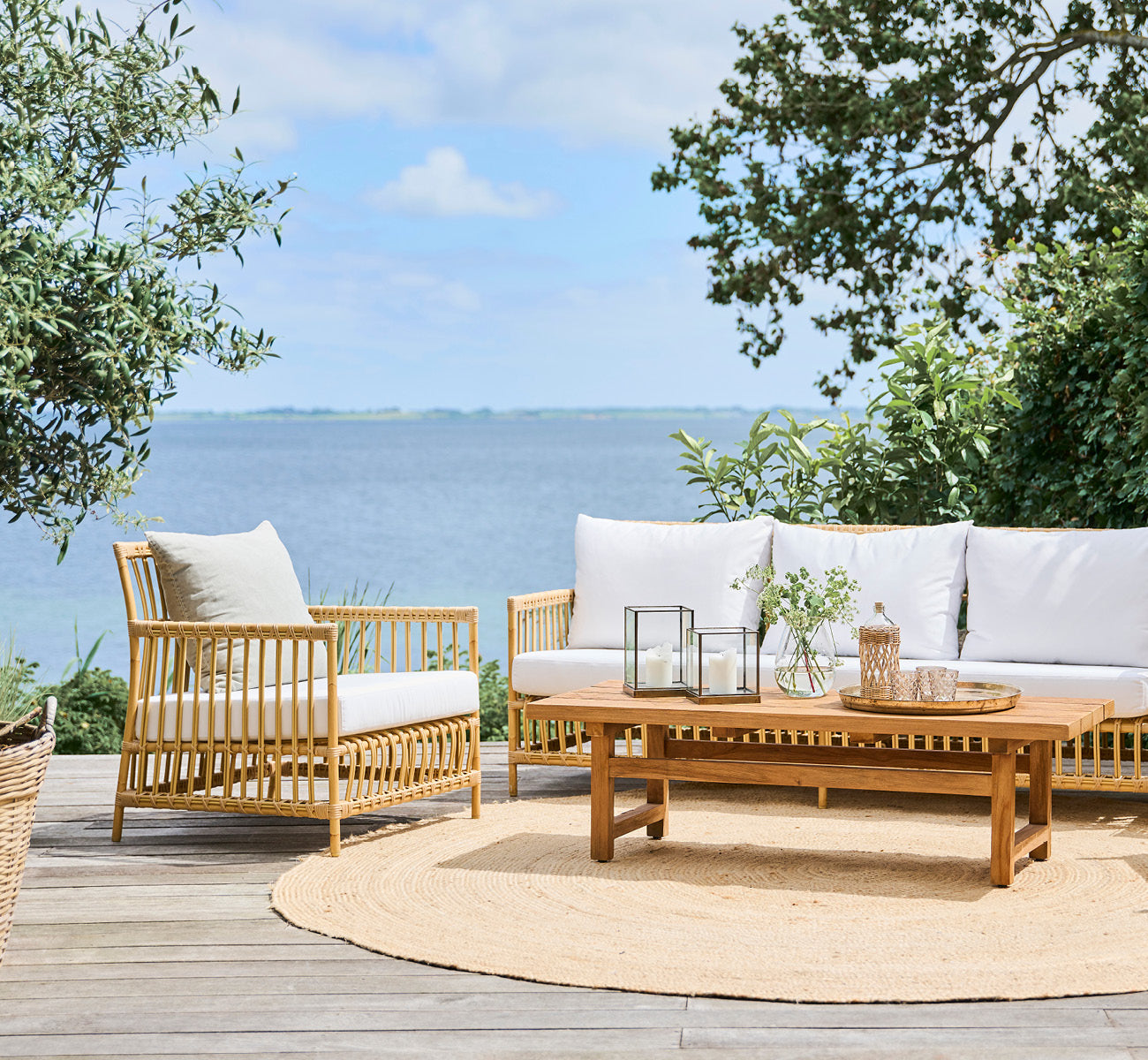 Esta es una imagen de estilo de vida de Caroline sillón lounge exterior en natural Aluminium ArtFibre, en una terraza de madera junto al agua con.