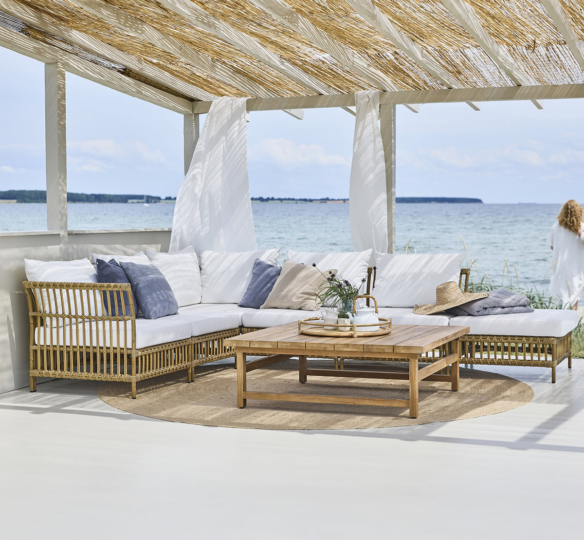 Esta es una imagen de estilo de vida de Maggie Sofá Módulo Central en antique aluminium artfibre. Pabellón de playa con sofá modular y vista al mar.