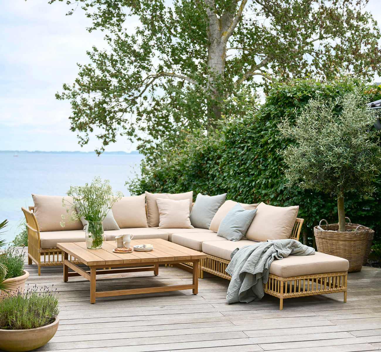 Esta es una imagen de estilo de vida de Maggie Sofá Módulo Puf c. Cristal en natural aluminium artfibre. Terraza junto al mar con sofá modular y manta drapeada.