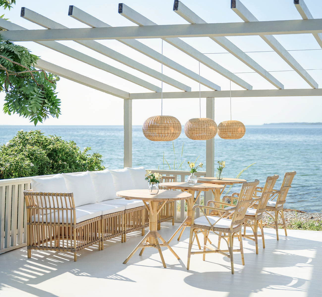 Esta es una imagen de estilo de vida de Meghan Exterior Dining Bench Corner Module i natural aluminium artfibre. En una terraza con pérgola junto al mar.