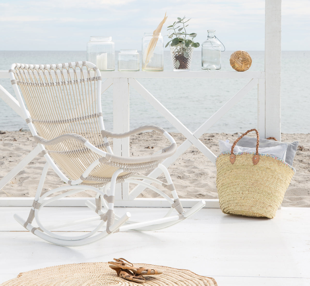 Esta es una imagen de estilo de vida de Monet Exterior Rocking Chair i dove white aluminium artfibre. En un pabellón de playa con vista al mar.