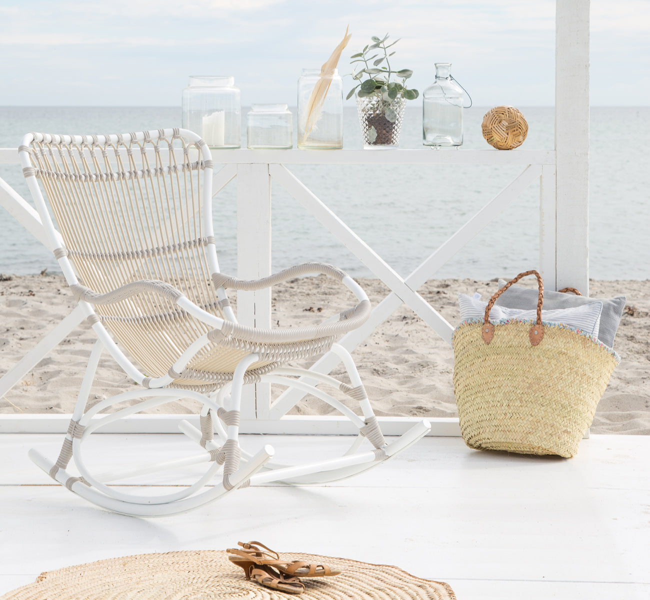 Esta es una imagen de estilo de vida de Monet Exterior Rocking Chair i dove white aluminium artfibre. En un pabellón de playa con vista al mar.