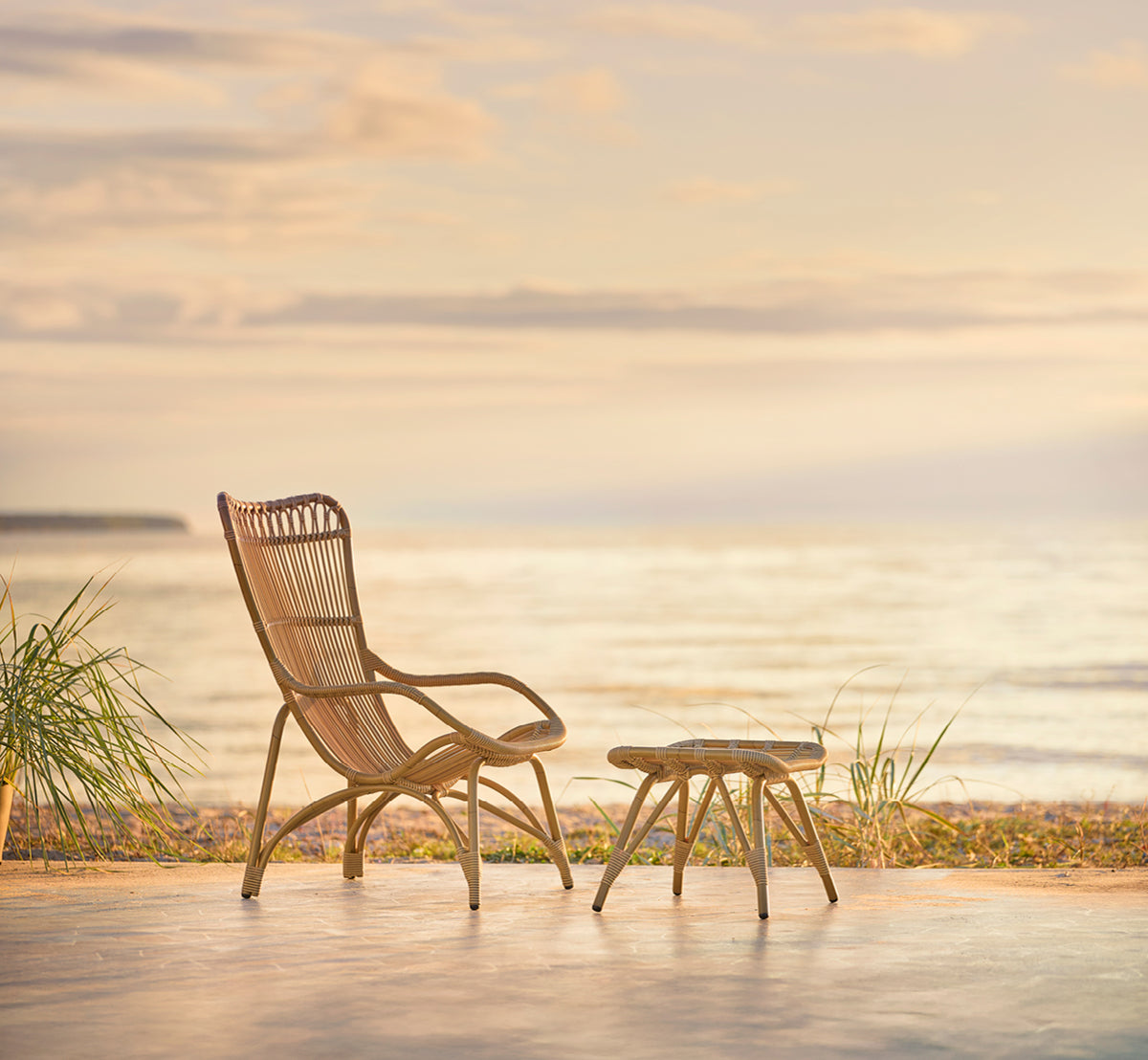 Esta es una imagen de estilo de vida de Monet Exterior Lounge Chair i antique aluminium artfibre. En un pabellón de playa con cortinas blancas.