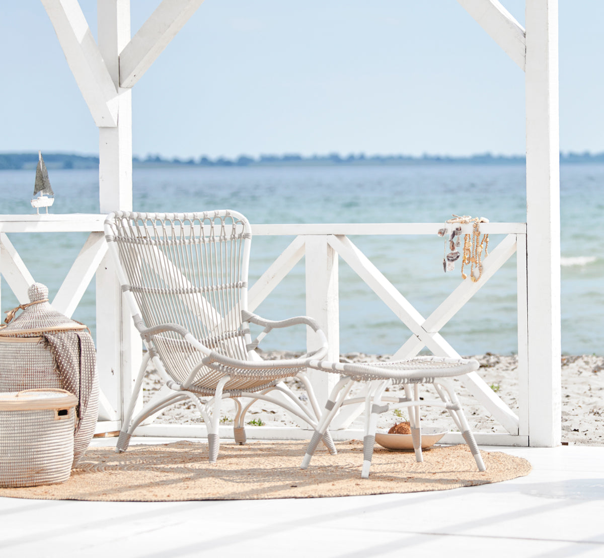 Esta es una imagen de estilo de vida de Monet Exterior Lounge Chair i dove white aluminium artfibre. En un pabellón de playa con alfombra de yute.