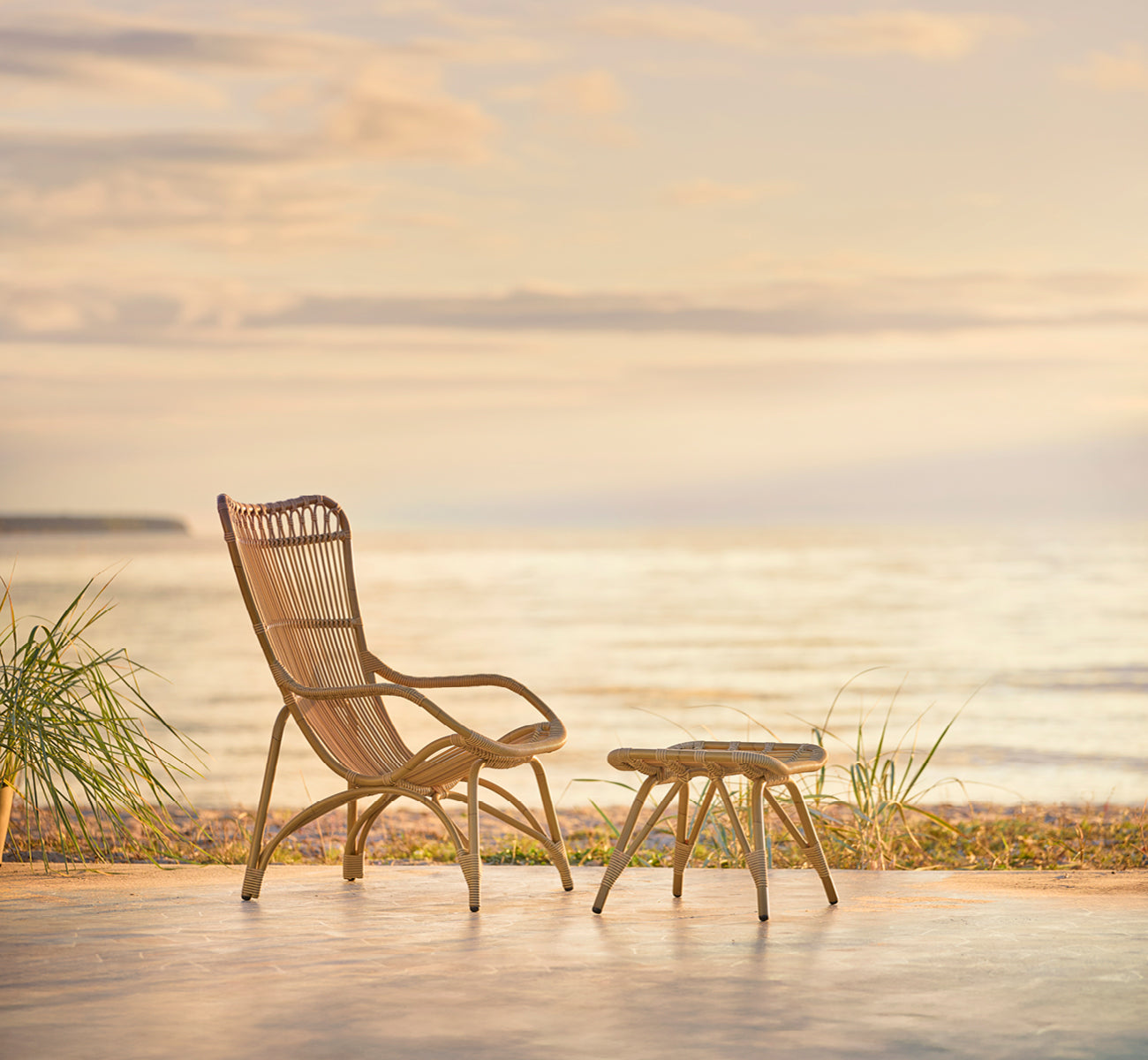 Esta es una imagen de estilo de vida de Monet Exterior Footstool i antique aluminium artfibre. Con sillón lounge en la terraza de un pabellón de playa.