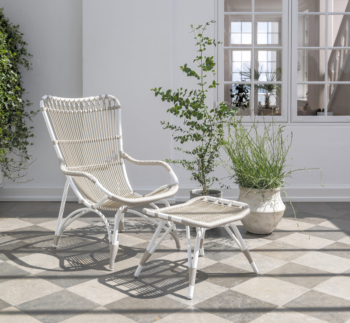 Esta es una imagen de estilo de vida de Monet Exterior Footstool i dove white aluminium artfibre. En un porche de playa con sillón lounge.