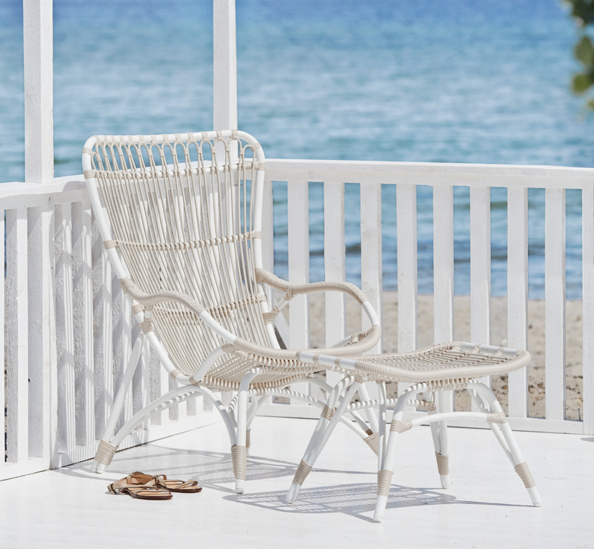 Esta es una imagen de estilo de vida de Monet Exterior Footstool i dove white aluminium artfibre. Con sillón lounge en un porche junto al mar.