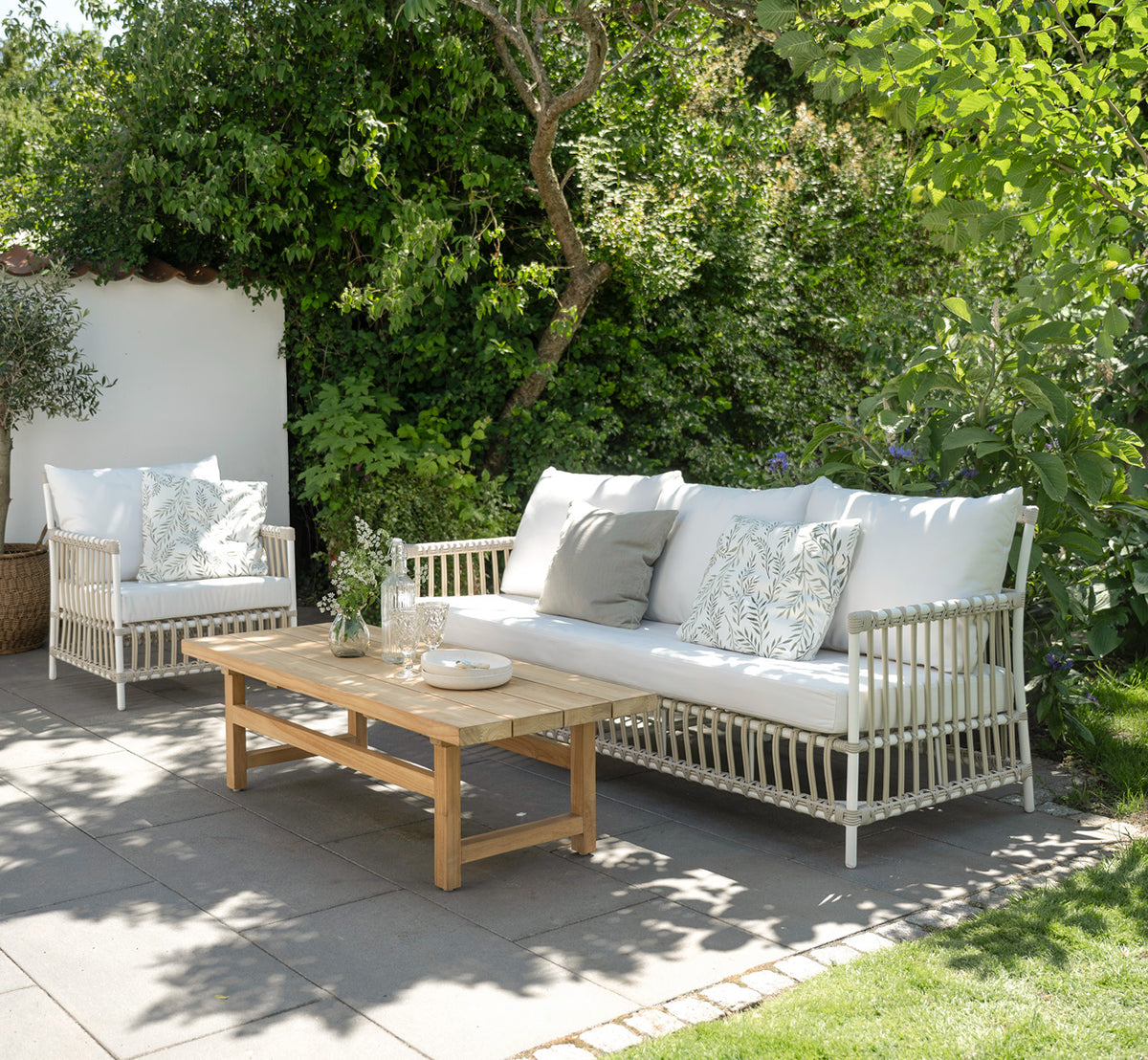 Esta es una imagen de estilo de vida de Caroline sofá exterior en dove White Aluminium ArtFibre, en una terraza de madera junto al agua con.