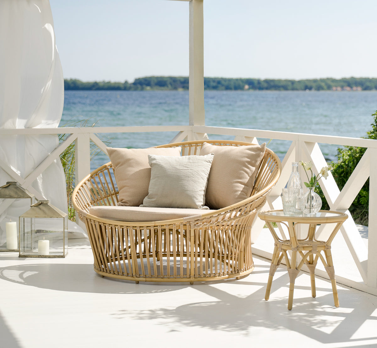 Esta es una imagen de estilo de vida de Tony Exterior Side Table i natural aluminium artfibre. En una terraza de madera con alfombra de yute junto al mar.