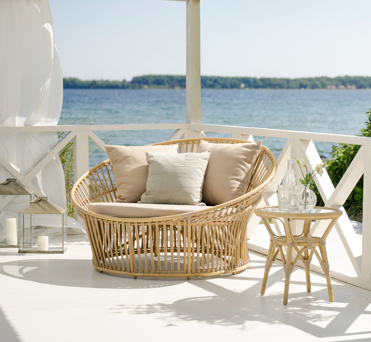 Esta es una imagen de estilo de vida de Tony Exterior Side Table i natural aluminium artfibre. En una terraza de madera con alfombra de yute junto al mar.