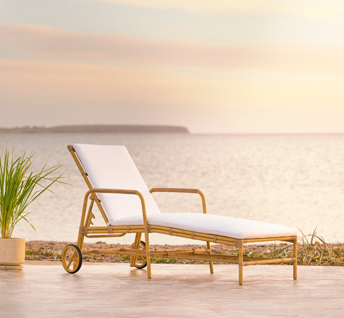 Esta es una imagen de estilo de vida de Josephine tumbona en natural aluminium artfibre, en una terraza costera de piedra al atardecer con vistas al.