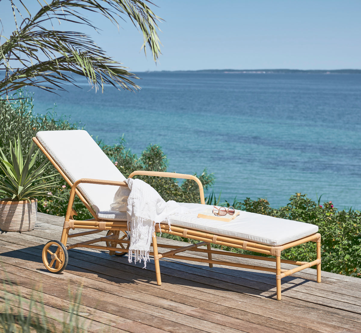 Esta es una imagen de estilo de vida de Josephine tumbona en natural aluminium artfibre, en una terraza costera de piedra al atardecer con vistas al.