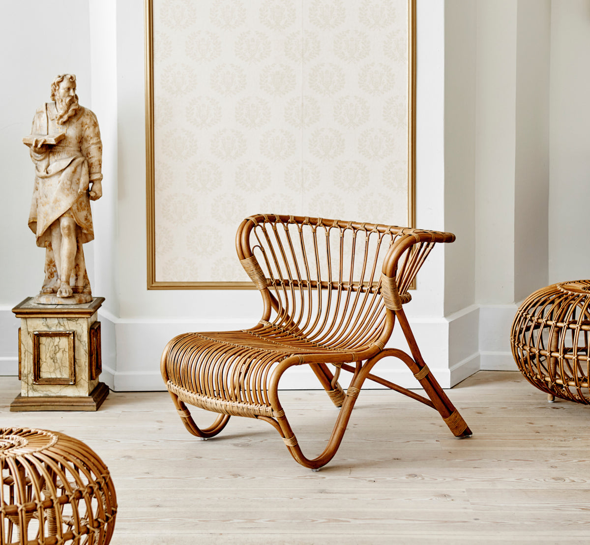 Esta es una imagen de estilo de vida de Fox sillón lounge en polished Antique Rattan, en un interior cálido con lambrisado ocre y parqué oscuro en.