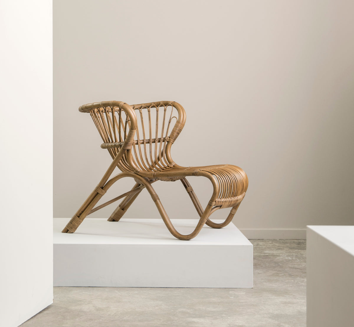 Esta es una imagen de estilo de vida de Fox sillón lounge en polished Antique Rattan, en un interior cálido con lambrisado ocre y parqué oscuro en.