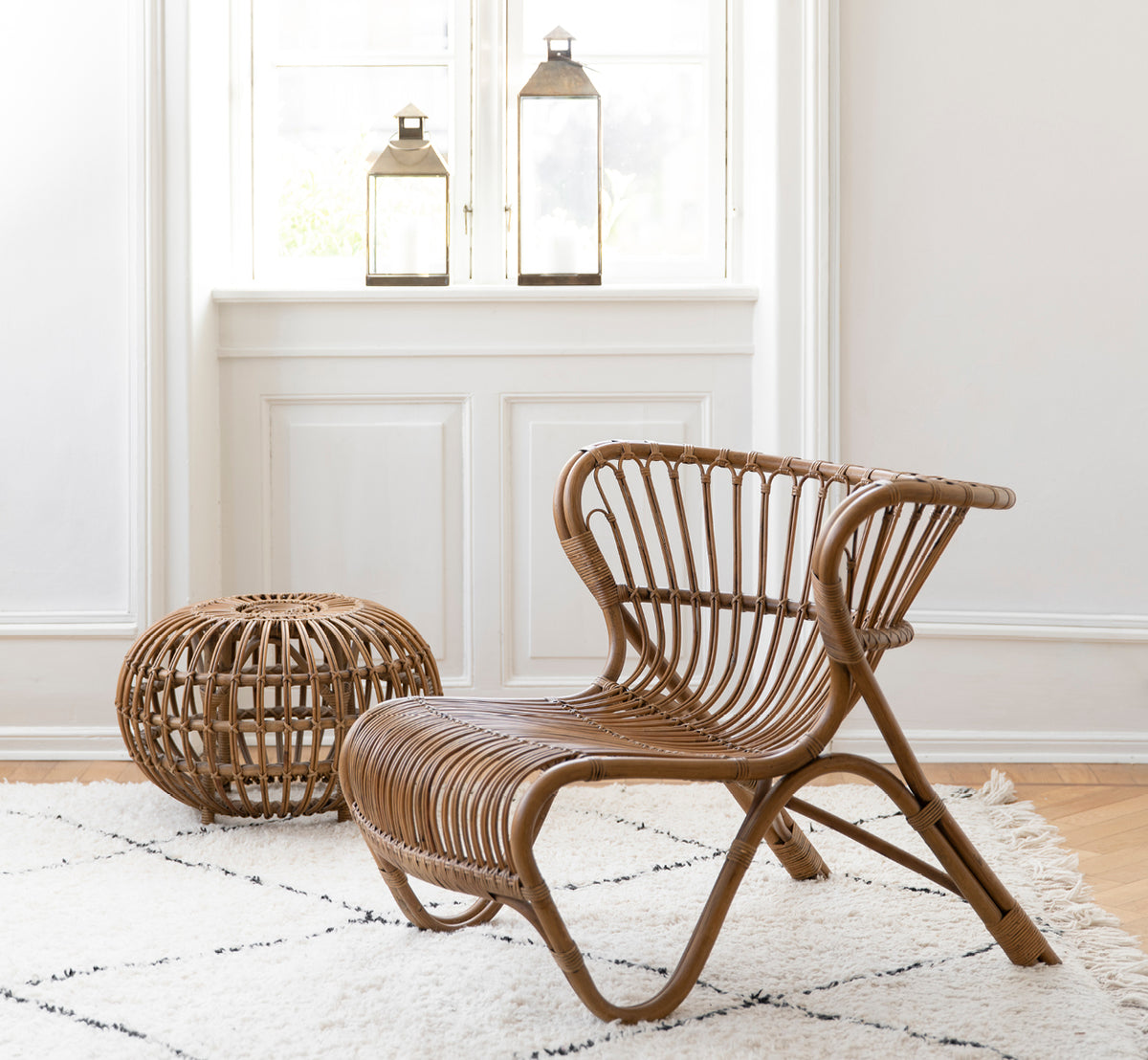 Esta es una imagen de estilo de vida de Fox sillón lounge en polished Antique Rattan, en un interior cálido con lambrisado ocre y parqué oscuro en.