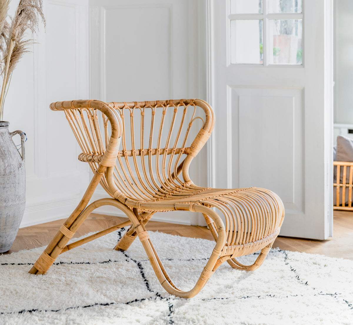 Esta es una imagen de estilo de vida de Fox sillón lounge en polished Natural Rattan, en un interior cálido con lambrisado ocre y parqué oscuro en.