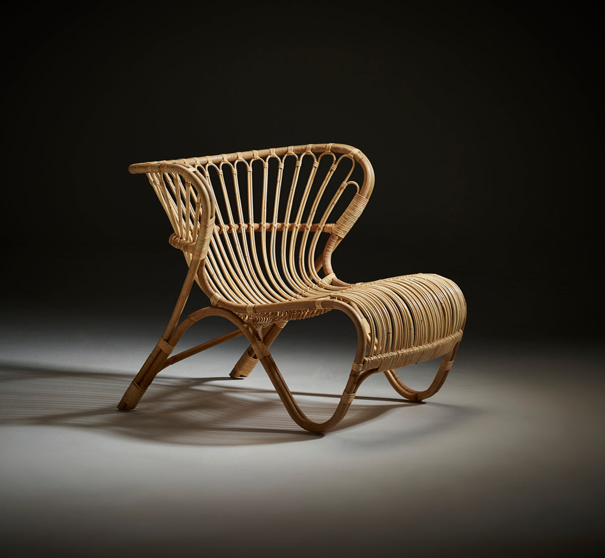 Esta es una imagen de estilo de vida de Fox sillón lounge en polished Natural Rattan, en un interior cálido con lambrisado ocre y parqué oscuro en.