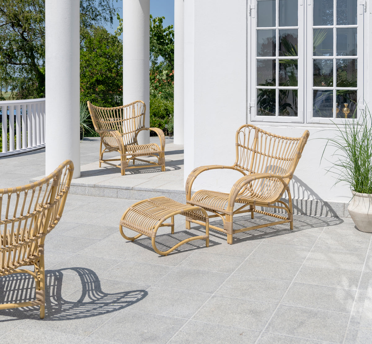 Esta es una imagen de estilo de vida de Teddy reposapiés exterior en natural aluminium artfibre. Combinado con el sillón lounge a juego en una terraza pavimentada soleada.