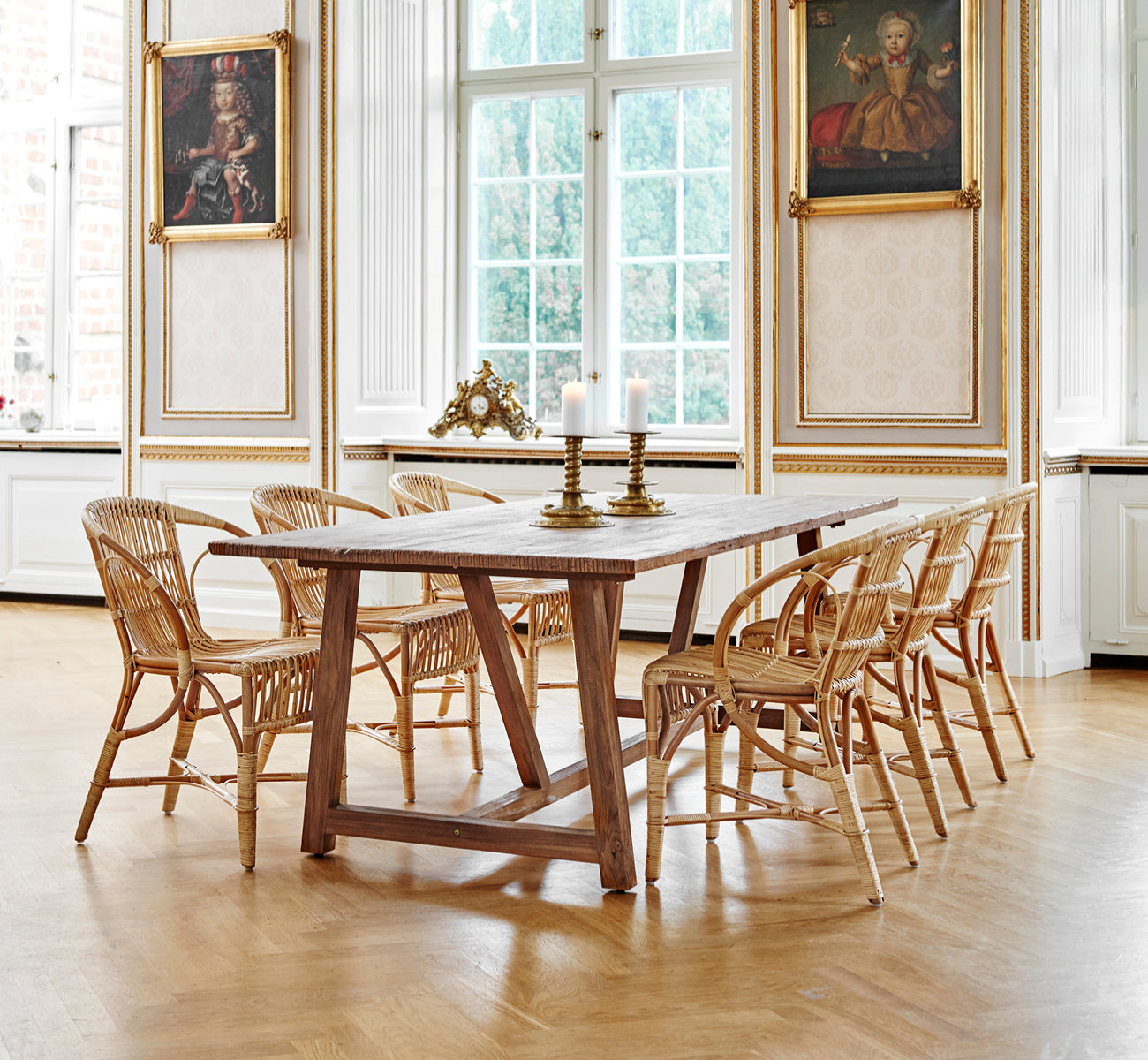 Esta es una imagen de estilo de vida de Robert silla de comedor en polished antique rattan. Colocada junto a una alta urna de terracota sobre un suelo de parqué en espiga.