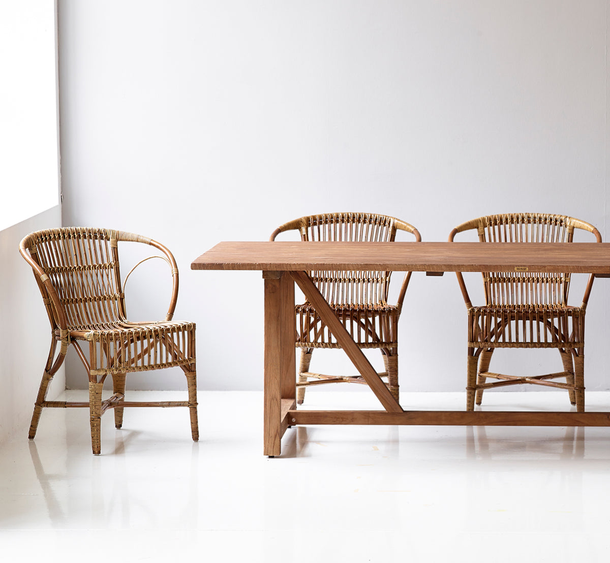 Esta es una imagen de estilo de vida de Robert silla de comedor en polished antique rattan. Colocada junto a una alta urna de terracota sobre un suelo de parqué en espiga.