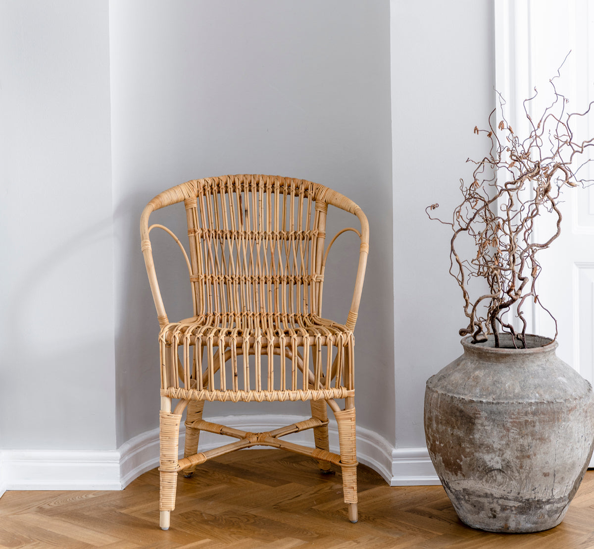 Esta es una imagen de estilo de vida de Robert silla de comedor en polished natural rattan. Colocada junto a una mesa de pedestal con tulipanes sobre una alfombra de yute.